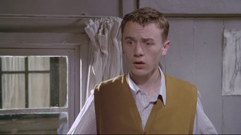 Movie still from “My Left Foot” (1989), directed by Jim Sheridan – A young man in a yellow vest looks at the camera; Close Up shot, Low angle