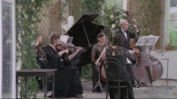 Movie still from “My Left Foot” (1989), directed by Jim Sheridan – A group of people playing musical instruments in a room; Wide shot, High angle