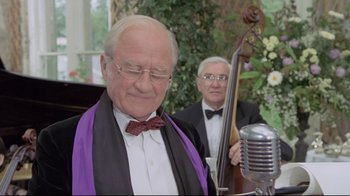 Movie still from “My Left Foot” (1989), directed by Jim Sheridan – A man in a bow tie is standing in front of a microphone and another man in a bow tie is standing in front of a microphone; Close Up shot, Over the shoulder angle