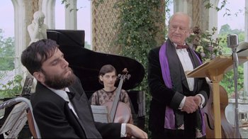Movie still from “My Left Foot” (1989), directed by Jim Sheridan – A group of men in suits and ties playing musical instruments; Medium shot, Over the shoulder angle