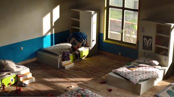Movie still from “My Life as a Zucchini” (2016), directed by Claude Barras – A doll sitting on a bed in a room with wooden floors; Wide shot, Overhead angle