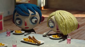 Movie still from “My Life as a Zucchini” (2016), directed by Claude Barras – A couple of figurines sitting next to each other at a table; Medium shot, High angle