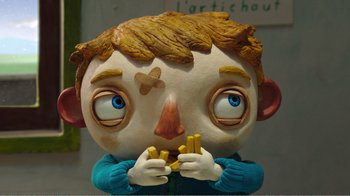 Movie still from “My Life as a Zucchini” (2016), directed by Claude Barras – The face of a sculpture of a boy holding bananas; Close Up shot, Overhead angle