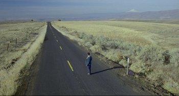 Movie still from “My Own Private Idaho” (1991), directed by Gus Van Sant – A man standing on the side of a road near a field; Extreme Wide shot, High angle