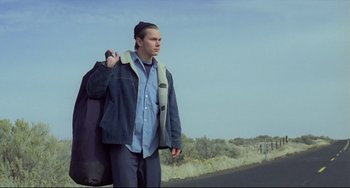 Movie still from “My Own Private Idaho” (1991), directed by Gus Van Sant – A young man holding a guitar case on the side of a road; Medium shot, Low angle
