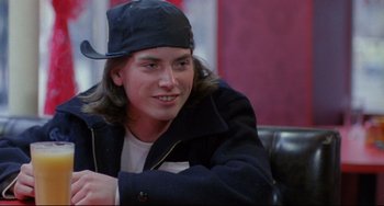 Movie still from “My Own Private Idaho” (1991), directed by Gus Van Sant – A young man sitting in a chair wearing a hat; Close Up shot, Over the shoulder angle