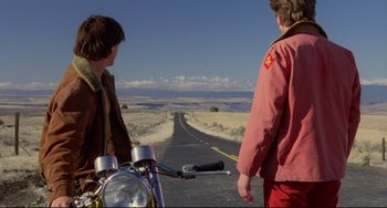 Movie still from “My Own Private Idaho” (1991), directed by Gus Van Sant – Two people standing on the side of a road with a motorcycle; Wide shot, Low angle