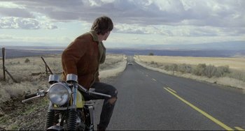 Movie still from “My Own Private Idaho” (1991), directed by Gus Van Sant – A man riding a motorcycle down the middle of a road; Wide shot, Low angle