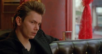 Movie still from “My Own Private Idaho” (1991), directed by Gus Van Sant – A young man with a black shirt and a black jacket sitting on a leather chair; Close Up shot, Over the shoulder angle