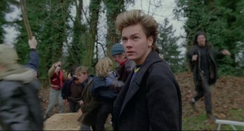 Movie still from “My Own Private Idaho” (1991), directed by Gus Van Sant – A young man standing in front of a group of people in a forest; Close Up shot, Over the shoulder angle