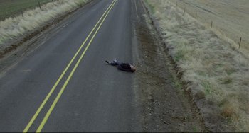 Movie still from “My Own Private Idaho” (1991), directed by Gus Van Sant – A man laying on the side of a road; Extreme Wide shot, Overhead angle