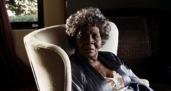 Movie still from “My Son, My Son, What Have Ye Done” (2009), directed by Werner Herzog – An older woman sitting in a chair looking at the camera; Close Up shot, Low angle