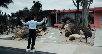 Movie still from “My Son, My Son, What Have Ye Done” (2009), directed by Werner Herzog – A man standing on the side of the road with his arms outstretched; Wide shot, Low angle