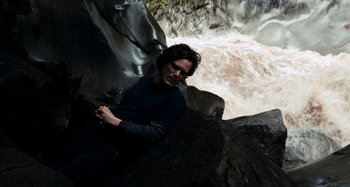 Movie still from “My Son, My Son, What Have Ye Done” (2009), directed by Werner Herzog – A man sitting on the side of a waterfall; Medium shot, High angle