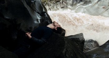 Movie still from “My Son, My Son, What Have Ye Done” (2009), directed by Werner Herzog – A man laying on the ground in front of a waterfall; Medium shot, High angle
