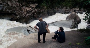 Movie still from “My Son, My Son, What Have Ye Done” (2009), directed by Werner Herzog – Two people sitting on a rock looking at a river; Wide shot, High angle
