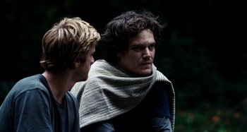 Movie still from “My Son, My Son, What Have Ye Done” (2009), directed by Werner Herzog – Two men standing next to each other in a wooded area; Close Up shot, Over the shoulder angle
