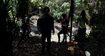 Movie still from “My Son, My Son, What Have Ye Done” (2009), directed by Werner Herzog – A group of people standing in the woods near a waterfall; Wide shot, Over the shoulder angle