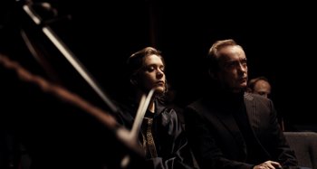 Movie still from “My Son, My Son, What Have Ye Done” (2009), directed by Werner Herzog – A man and a woman sitting next to each other in a dark room; Medium shot, Low angle