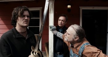 Movie still from “My Son, My Son, What Have Ye Done” (2009), directed by Werner Herzog – A man holding a sword in front of two other men; Medium shot, Over the shoulder angle