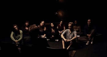 Movie still from “My Son, My Son, What Have Ye Done” (2009), directed by Werner Herzog – A group of people sitting in a dark room; Wide shot, High angle