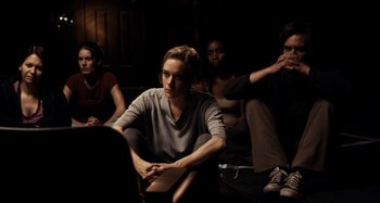 Movie still from “My Son, My Son, What Have Ye Done” (2009), directed by Werner Herzog – A group of people sitting in a dark room; Medium shot, High angle
