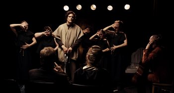 Movie still from “My Son, My Son, What Have Ye Done” (2009), directed by Werner Herzog – A group of people standing around a man holding a sword; Wide shot, Over the shoulder angle