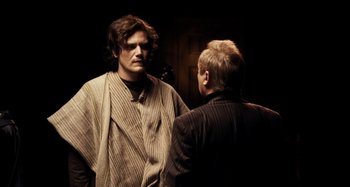 Movie still from “My Son, My Son, What Have Ye Done” (2009), directed by Werner Herzog – A man standing next to another man in a room; Medium shot, Over the shoulder angle