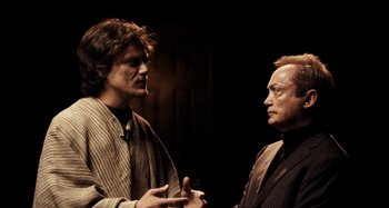 Movie still from “My Son, My Son, What Have Ye Done” (2009), directed by Werner Herzog – Two men talking to each other in front of a dark background; Medium shot, Over the shoulder angle