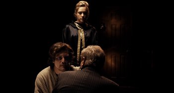 Movie still from “My Son, My Son, What Have Ye Done” (2009), directed by Werner Herzog – A man and a woman in a dark room with another man; Medium shot, Over the shoulder angle