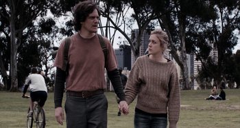 Movie still from “My Son, My Son, What Have Ye Done” (2009), directed by Werner Herzog – A man and a woman holding hands while standing on the grass; Medium shot, Low angle