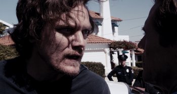 Movie still from “My Son, My Son, What Have Ye Done” (2009), directed by Werner Herzog – A person near a police officer; Close Up shot, Over the shoulder angle