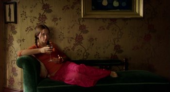 Movie still from “My Summer of Love” (2004), directed by Pawel Pawlikowski – A woman in a red dress is sitting on the ground holding a glass of wine; Medium shot, High angle