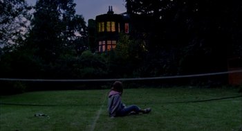 Movie still from “My Summer of Love” (2004), directed by Pawel Pawlikowski – A person sitting on the grass in front of a building; Extreme Wide shot, Low angle