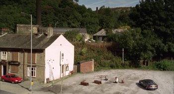 Movie still from “My Summer of Love” (2004), directed by Pawel Pawlikowski – Two people sitting in a parking lot next to a house; Extreme Wide shot, High angle