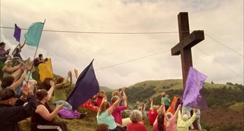 Movie still from “My Summer of Love” (2004), directed by Pawel Pawlikowski – A group of people sitting in a field with a cross in the background; Extreme Wide shot, High angle