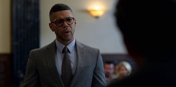 Movie still from “13 Reasons Why” (2017), created by Brian Yorkey – A man in a suit and tie standing in front of a group of people; Close Up shot, Over the shoulder angle