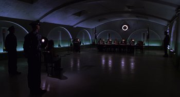 Movie still from “Mystery Men” (1999), directed by Kinka Usher – A group of people sitting at a table in a dark room; Extreme Wide shot, High angle