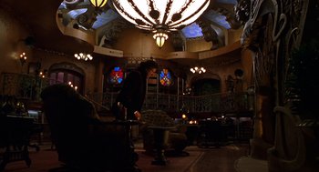 Movie still from “Mystery Men” (1999), directed by Kinka Usher – A man standing in front of a table in a room with stained - glass windows; Wide shot, Low angle