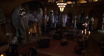 Movie still from “Mystery Men” (1999), directed by Kinka Usher – A man sitting on a chair in a room; Wide shot, High angle