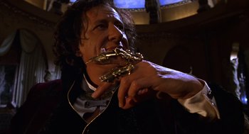 Movie still from “Mystery Men” (1999), directed by Kinka Usher – A man holding a pair of golden statues in his mouth; Close Up shot, Low angle