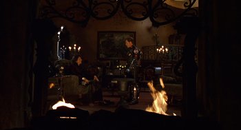 Movie still from “Mystery Men” (1999), directed by Kinka Usher – Two people sitting in a living room next to a fireplace; Wide shot, High angle