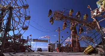 Movie still from “Mystery Men” (1999), directed by Kinka Usher – An amusement park with a car parked in front of it; Extreme Wide shot, Low angle