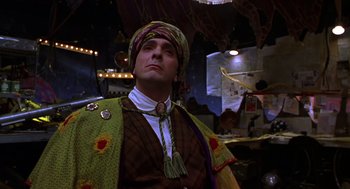 Movie still from “Mystery Men” (1999), directed by Kinka Usher – A man wearing a colorful outfit in a dark room; Medium shot, Low angle