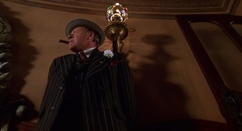 Movie still from “Mystery Men” (1999), directed by Kinka Usher – A man in a suit and hat smoking a cigar; Medium shot, Low angle