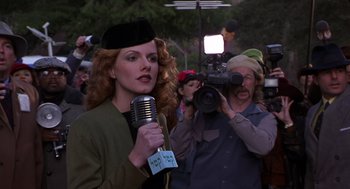 Movie still from “Mystery Men” (1999), directed by Kinka Usher – A woman holding a microphone in front of a camera; Medium shot, Low angle