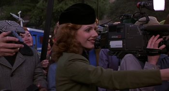 Movie still from “Mystery Men” (1999), directed by Kinka Usher – A woman in a black hat and a green jacket is standing in front of a camera; Close Up shot, Over the shoulder angle