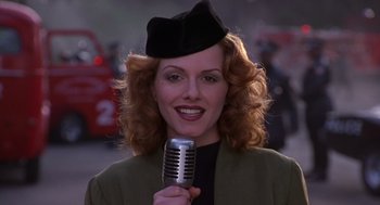 Movie still from “Mystery Men” (1999), directed by Kinka Usher – A woman in a hat holding up a microphone; Close Up shot, Low angle