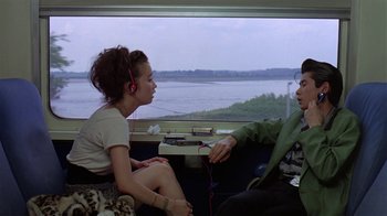 Movie still from “Mystery Train” (1989), directed by Jim Jarmusch – Two people are sitting on a train looking at each other; Medium shot, Over the shoulder angle