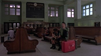 Movie still from “Mystery Train” (1989), directed by Jim Jarmusch – A man sitting on a bench next to a red suitcase; Wide shot, High angle